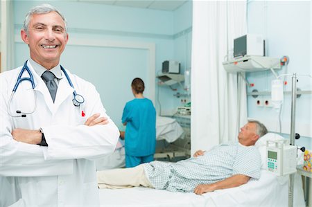 simsearch:6109-06196363,k - Smiling doctor with his arms folded standing in a bed ward Stock Photo - Premium Royalty-Free, Code: 6109-06196271