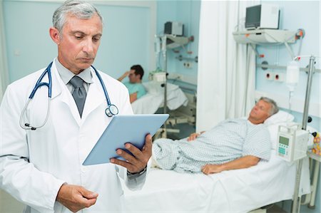 simsearch:6109-06196363,k - Doctor holding a tactile tablet while standing in a bed ward Stock Photo - Premium Royalty-Free, Code: 6109-06196278