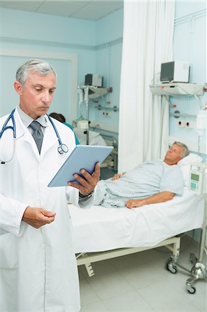 simsearch:6109-06196363,k - Serious doctor holding a tactile tablet while standing Stock Photo - Premium Royalty-Free, Code: 6109-06196279