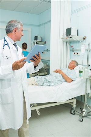 simsearch:6109-06196363,k - Serious doctor using a tactile tablet while looking at a patient in a bed ward Stock Photo - Premium Royalty-Free, Code: 6109-06196287