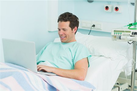 simsearch:6109-06196332,k - Smiling patient using a laptop while lying on a bed Foto de stock - Sin royalties Premium, Código: 6109-06196297
