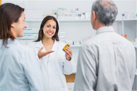 Pharmacist presenting a bottle of pills behind the counter of a pharmacy Stock Photo - Premium Royalty-Free, Code: 6109-06196224