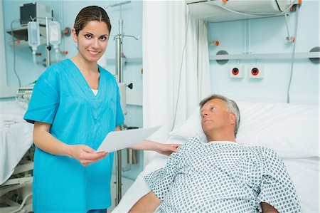 simsearch:6109-06196363,k - Smiling nurse touching the shoulder of a patient lying on a bed while holding a paper Stock Photo - Premium Royalty-Free, Code: 6109-06196353