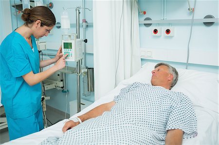 simsearch:6109-06196332,k - Nurse checking a medical machine next to a patient lying on a bed Foto de stock - Sin royalties Premium, Código: 6109-06196350