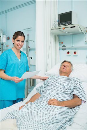 simsearch:6109-06196363,k - Smiling nurse touching the shoulder of a male patient lying on a bed while holding a paper Stock Photo - Premium Royalty-Free, Code: 6109-06196355