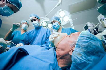 Surgerical team in an operating theater operating an unconscious patient Foto de stock - Sin royalties Premium, Código: 6109-06196386