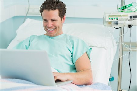 simsearch:6109-06196332,k - Happy male patient typing on a laptop while lying on a bed Foto de stock - Sin royalties Premium, Código: 6109-06196312