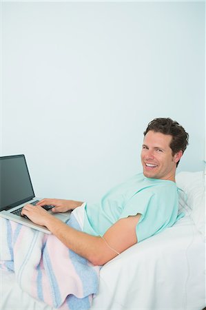 simsearch:6109-06196332,k - Male patient using a laptop while laying on a bed Foto de stock - Sin royalties Premium, Código: 6109-06196318