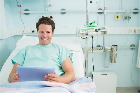simsearch:6109-06196332,k - Male patient holding a tactile tablet while lying on a bed Foto de stock - Sin royalties Premium, Código: 6109-06196323