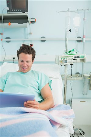 simsearch:6109-06196332,k - Smiling male patient using a tactile tablet while lying on a bed Foto de stock - Sin royalties Premium, Código: 6109-06196321