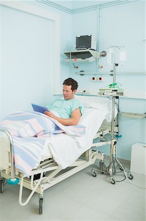 simsearch:6109-06196332,k - Focus male patient holding a tactile tablet while lying on a bed Foto de stock - Sin royalties Premium, Código: 6109-06196327