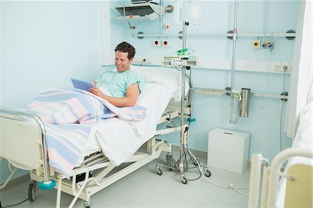 simsearch:6109-06196332,k - Smiling male patient holding a tactile tablet while lying on a bed Foto de stock - Sin royalties Premium, Código: 6109-06196326