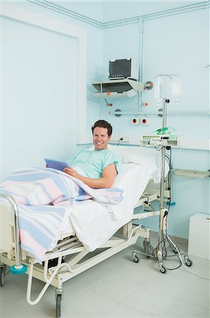 simsearch:6109-06196332,k - Joyful male patient holding a tactile tablet while lying on a bed Foto de stock - Sin royalties Premium, Código: 6109-06196328