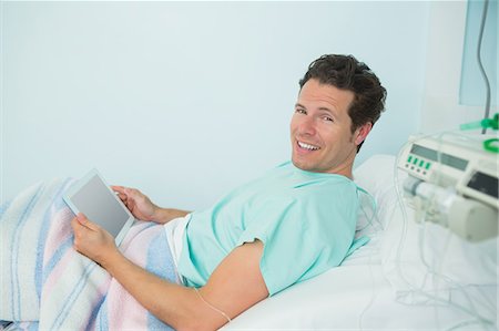 simsearch:6109-06196332,k - Smiling male patient touching a tactile tablet while lying on a bed Foto de stock - Sin royalties Premium, Código: 6109-06196331