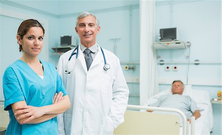 simsearch:6109-06196363,k - Doctor and nurse with her arms crossed standing in the room of a patient Stock Photo - Premium Royalty-Free, Code: 6109-06196337