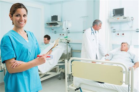 simsearch:6109-06196363,k - Smiling nurse holding a file while standing in a bed ward Stock Photo - Premium Royalty-Free, Code: 6109-06196334