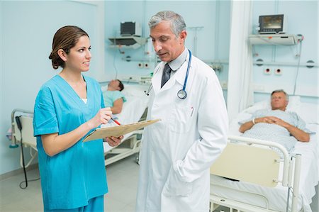 simsearch:6109-06196363,k - Doctor and a smiling nurse talking in a hospital with two patients Stock Photo - Premium Royalty-Free, Code: 6109-06196339