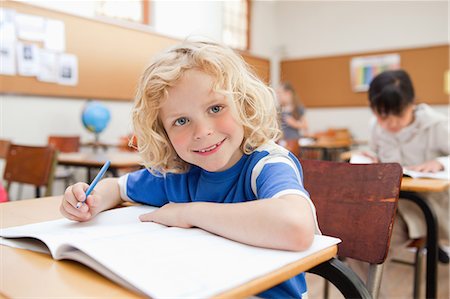 Smiling schoolboy sitting at desk with exercise book Stock Photo - Premium Royalty-Free, Code: 6109-06196537
