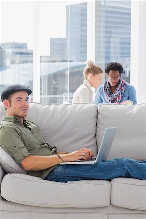 Cheerful worker using his laptop while laying on a couch Stock Photo - Premium Royalty-Free, Code: 6109-06781503
