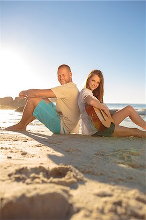 sunrise with couple - Smiling sat back to back on the beach Stock Photo - Premium Royalty-Free, Code: 6109-06781679