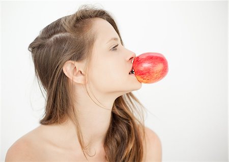 Pretty woman holding a red apple by biting the stalk Stock Photo - Premium Royalty-Free, Code: 6109-06781847