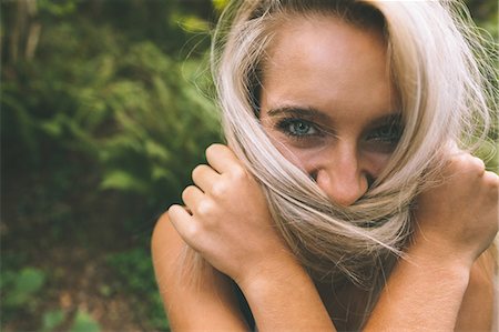 Happy gorgeous blonde covering her mouth with hair in the woods Stock Photo - Premium Royalty-Free, Code: 6109-07497113