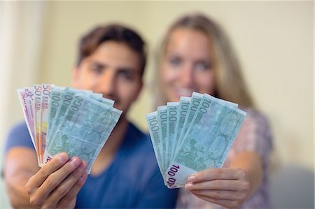 Cheerful couple showing money smiling at camera at home on the couch Stock Photo - Premium Royalty-Free, Code: 6109-07497371