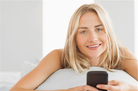 simsearch:6109-07497311,k - Smiling blonde lying on her pillow sending a text at home in bedroom Stock Photo - Premium Royalty-Free, Code: 6109-07497394