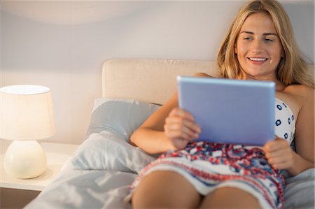 simsearch:6109-07497438,k - Happy woman wearing dress lying on bed with her tablet pc at home in bedroom Stock Photo - Premium Royalty-Free, Code: 6109-07497424