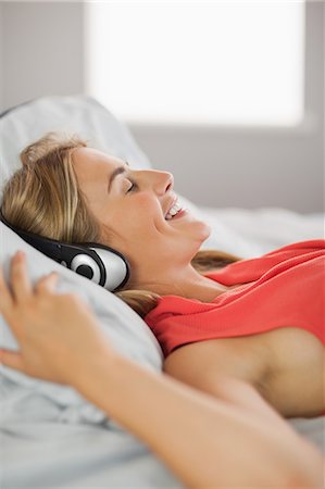 simsearch:6109-07497438,k - Content blonde wearing dress lying on bed listening to music at home in bedroom Stock Photo - Premium Royalty-Free, Code: 6109-07497431