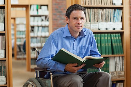 Content man in wheelchair holding a book in library in a college Stock Photo - Premium Royalty-Free, Code: 6109-07497503