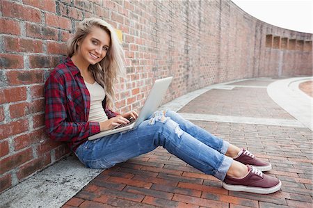 Cheerful gorgeous student leaning against wall using laptop on college campus Stock Photo - Premium Royalty-Free, Code: 6109-07497518