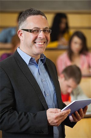 Lecturer holding tablet pc in front of class in lecture hall smiling at camera in college Stock Photo - Premium Royalty-Free, Code: 6109-07497675