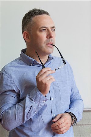 Thoughtful lecturer standing in his classroom biting his glasses in college Stock Photo - Premium Royalty-Free, Code: 6109-07497631