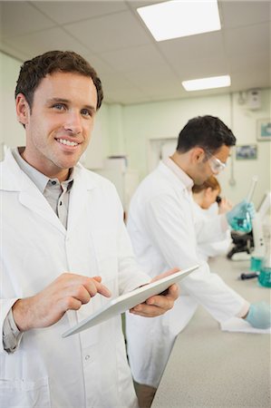 science lab - Handsome young scientist using his tablet while standing in the laboratory and smiling at camera Stock Photo - Premium Royalty-Free, Code: 6109-07497776