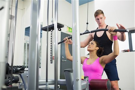 simsearch:6109-07497839,k - Instructor assisting fit brunette at weight machine in weights room of gym Stock Photo - Premium Royalty-Free, Code: 6109-07497845