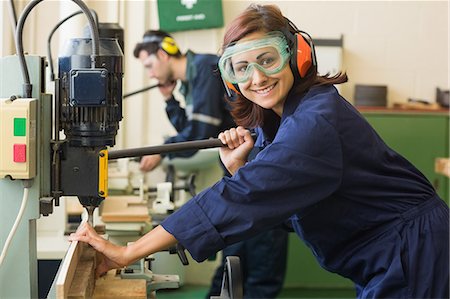 simsearch:400-07899762,k - Smiling trainee with safety glasses drilling wood in workshop Stock Photo - Premium Royalty-Free, Code: 6109-07497988