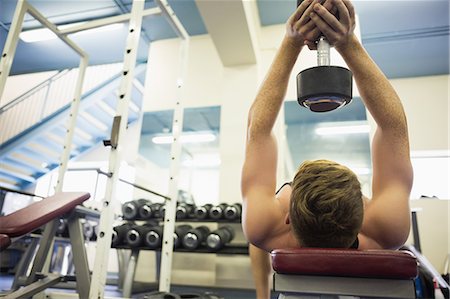 Muscular man holding heavy dumbbell over head in weights room of gym Stock Photo - Premium Royalty-Free, Code: 6109-07497904