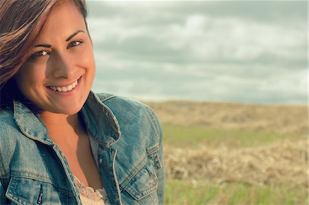 Close up portrait of a beautiful smiling young woman at cereal field against cloudy sky Stock Photo - Premium Royalty-Free, Code: 6109-07498094