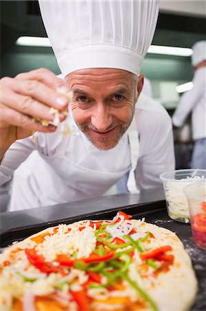 Happy chef sprinkling cheese on a pizza Photographie de stock - Premium Libres de Droits, Code: 6109-07601099