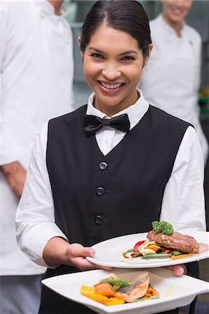 food and beverages hotel uniforms - Happy waitress holding steak dinner and salmon dinner Stock Photo - Premium Royalty-Free, Code: 6109-07601133