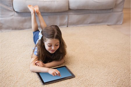 Full length of a little girl using digital tablet in living room Stock Photo - Premium Royalty-Free, Code: 6109-07601507