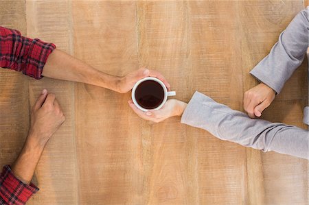 person holding cup of coffee - Two hands holding a cup of coffee on wooden table Stock Photo - Premium Royalty-Free, Code: 6109-08203255