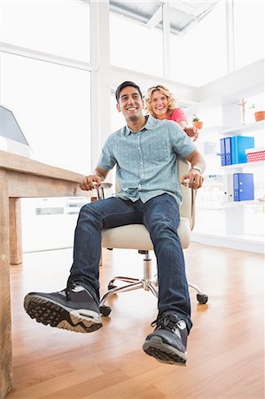 simsearch:6109-08203934,k - Smiling colleagues playing together with swivel chair Stock Photo - Premium Royalty-Free, Code: 6109-08203918