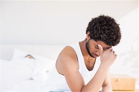 Troubled man sitting on bed in foreground Stock Photo - Premium Royalty-Free, Code: 6109-08390413