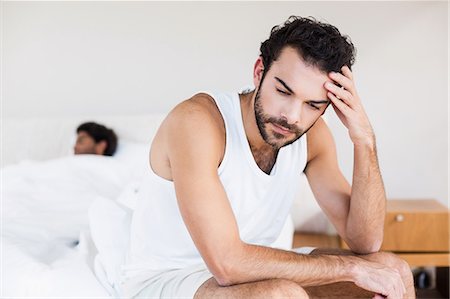 Troubled man sitting on bed in foreground Stock Photo - Premium Royalty-Free, Code: 6109-08390411