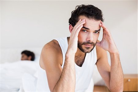 Troubled man sitting on bed in foreground Stock Photo - Premium Royalty-Free, Code: 6109-08390412