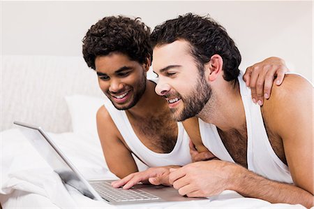 Happy gay couple laying on bed using laptop Stock Photo - Premium Royalty-Free, Code: 6109-08390419