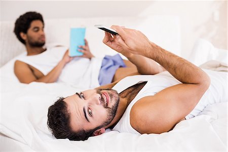 Smiling man using smartphone while partner reading book in background Stock Photo - Premium Royalty-Free, Code: 6109-08390421