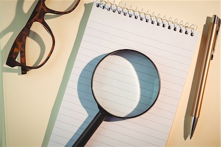 simsearch:6109-08395080,k - Magnifying glass on notepad amidst pen and eyeglasses Stock Photo - Premium Royalty-Free, Code: 6109-08395093